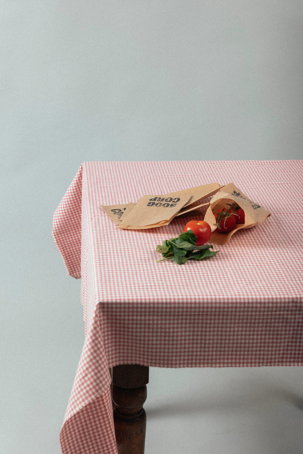 Tomates et basilic avec des sacs en papier 500GCORP sur une nappe à carreaux.